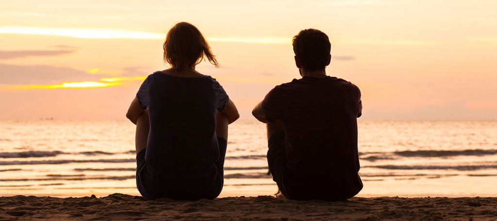 Two young people sitting on the beach together at sunset