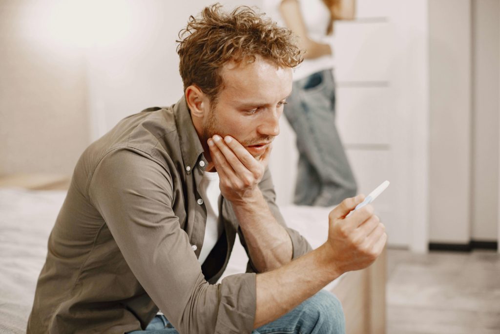 A man is seated on the floor, his hand placed over his mouth, suggesting deep thought or astonishment